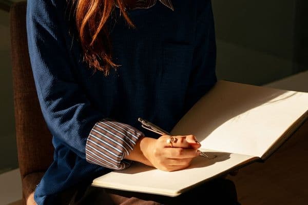 Kucağındaki açık deftere not alan, lacivert kazaklı bir terapistin el detay planı