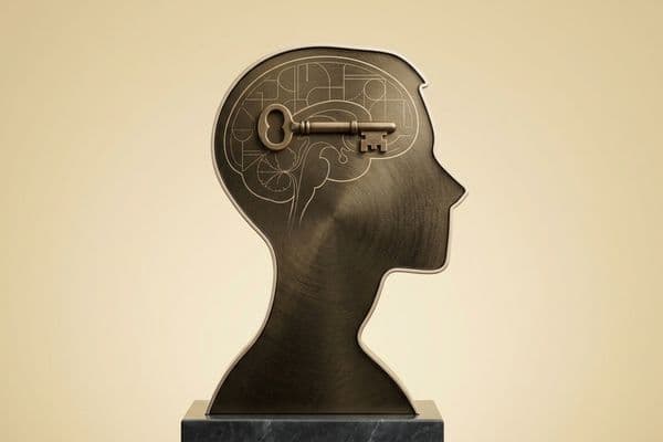 Krem rengi arka planda, üzerinde beyin kıvrımları ve geometrik şemalar çizili olan bronz bir insan başı silüeti ve zihnin merkezine yerleştirilmiş antik bir anahtar illüstrasyonu.
